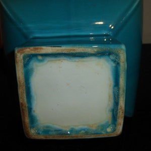 Pode incluir: Um vaso de cer&acirc;mica turquesa com base quadrada. A base tem um interior branco esmaltado e um exterior turquesa esmaltado.
