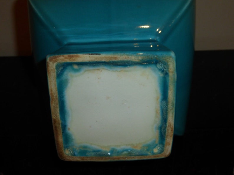 Pode incluir: Um vaso de cer&acirc;mica turquesa com base quadrada. A base tem um interior branco esmaltado e um exterior turquesa esmaltado.