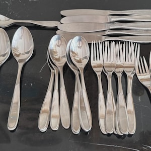 May include: A selection of stainless steel cutlery, comprising forks, spoons, and knives. The utensils are displayed on a dark surface, highlighting their polished, reflective appearance. The set includes various sizes of forks, spoons, and knives, ideal for a formal dining occasion.