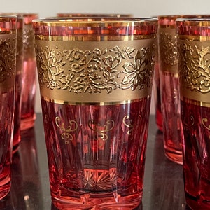 Puede incluir: Juego de seis vasos de vidrio rojo con ribetes dorados y diseños florales. Los vasos tienen un diseño facetado y una base transparente.