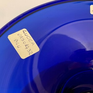 Puede incluir: Un cuenco de vidrio azul oscuro con una etiqueta que dice "Lucca Vaso 4332 Blu". El cuenco tiene el n&uacute;mero "4132" escrito en el lateral.