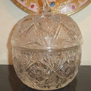 May include: A clear glass candy dish shaped like an apple with a decorative, cut-glass design. The lid has a knob in the shape of an apple stem.
