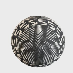 Könnte beinhalten: Ein kugelförmiges Keramikgefäß mit einem kontrastreichen schwarz-weißen geometrischen Muster. Die Oberfläche ist mit komplizierten, fein gezeichneten Sternmotiven und sich wiederholenden dreieckigen Formen verziert, die die runde Form umschließen.