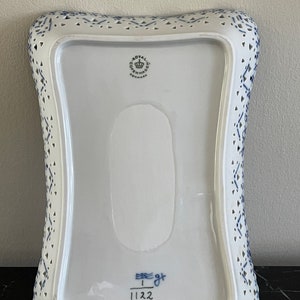 May include: A white ceramic serving dish with a blue and white pattern. The dish has a scalloped edge and a cut-out design. The bottom of the dish has the Royal Copenhagen logo and the number 1122.