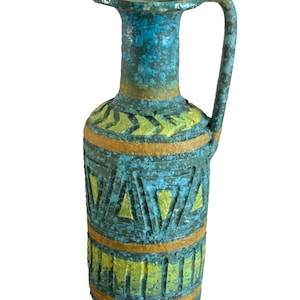 May include: A turquoise and yellow ceramic vase with a handle. The vase features geometric patterns and a textured surface. The design includes yellow triangles and horizontal bands, with a weathered appearance. The vase is approximately 10 inches tall.