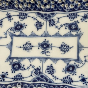May include: A white ceramic serving dish with a blue and white floral pattern. The dish has a scalloped edge and a raised rim.