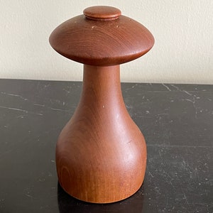 May include: A wooden mushroom-shaped salt and pepper shaker set. The shaker is made of dark brown wood and has a smooth, polished finish.