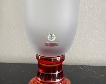 Puede incluir: Una copa de vidrio esmerilado con una base a rayas rojas y naranjas. La copa tiene una etiqueta que dice "Sax Glas Bruch Hand gebläsen spülmaschinenfest".