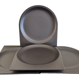 May include: Set of four dark gray ceramic plates. The plates are round with a slightly curved edge. The plates are stacked on top of each other.