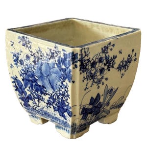Könnte beinhalten: Ein quadratischer Keramiktopf mit einem blauen und weißen Blumendesign. Der Topf hat vier Füße und eine breite Öffnung.