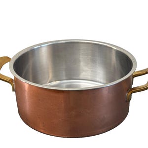 Puede incluir: Una olla de cocina de color cobre con interior de acero inoxidable y asas de latón. La olla es redonda con una amplia abertura, adecuada para diversas tareas culinarias. Las asas son curvas y están unidas a los lados.