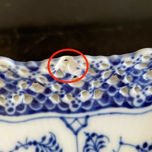 May include: Close-up of a blue and white porcelain plate with a scalloped edge. The edge of the plate has a delicate openwork design with a small chip on the rim.