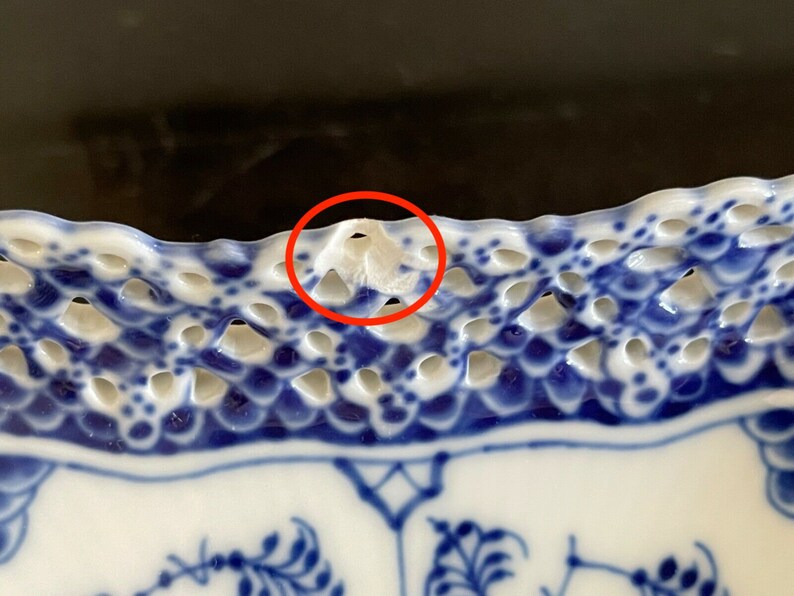 May include: Close-up of a blue and white porcelain plate with a scalloped edge. The edge of the plate has a delicate openwork design with a small chip on the rim.