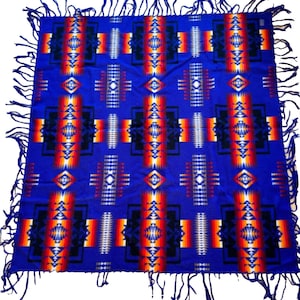 May include: A blue and red patterned blanket with fringe on all sides. The blanket has a geometric design with black, white, orange, and yellow accents.