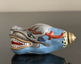 May include: A small, blue and white porcelain bottle with a dragon head design. The dragon has a red and orange mane and a gold stopper. The bottle is decorated with intricate details and is a unique piece of art.