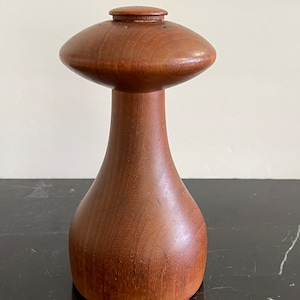 May include: A wooden salt and pepper shaker set in the shape of a mushroom. The shaker is made of dark brown wood and has a smooth, polished finish.