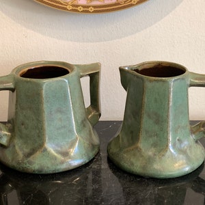 Pode incluir: Um conjunto de açucareiro e jarra de creme de cerâmica verde esmaltada com desenhos geométricos e alças quadradas.
