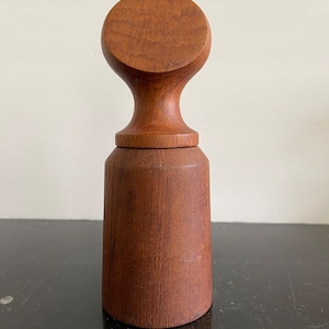 May include: A wooden salt and pepper shaker set with a unique design. The shakers are made of dark brown wood and have a rounded, cylindrical shape. The top of each shaker is a flat, circular disc with a small knob on top.