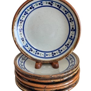 May include: A set of ceramic plates with a cream-coloured centre and a blue and green floral design around the rim. The plates have a brown border and are stacked on top of each other.
