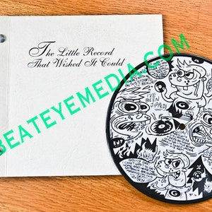 Op de afbeelding: Een zwart-witte 7-inch vinylplaat met een cartoonillustratie van een personage dat een draaitafel vasthoudt. De tekst "The Little Record That Wished It Could" is gedrukt op het platenlabel. De tekst "I've Been Jipped" is ook gedrukt op de plaat.