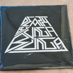 May include: Black vinyl record with a white triangle design. The text "Death By Bunga Bunga" is printed in white inside the triangle.