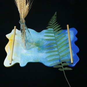 May include: A blue and yellow resin tray with gold handles. The tray has a wavy edge and is decorated with a fern and a glass vase with wheat.