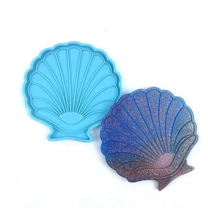 May include: A blue silicone mold shaped like a seashell, next to a finished resin seashell with a blue and purple glitter finish.