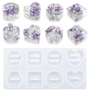 Può includere: Un set di otto espositori per anelli in resina trasparente con fiori secchi e uno stampo in silicone con otto forme di espositore per anelli. Le forme includono un cerchio, un quadrato, un cuore e un esagono.