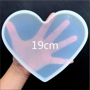 May include: A clear, heart-shaped silicone mould, measuring approximately 19cm across, is held up against a dark background. The number "19cm" is printed in white on the mould, indicating its size.