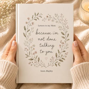 May include: A white hardcover book titled Letters to my Mom with the text because i'm not done talking to you and Love, Hayley printed on the front cover. The text is surrounded by a delicate botanical wreath illustration in muted green and pink.