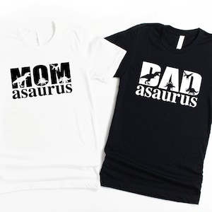 May include: Two t-shirts, one white and one black, with the text "Mom asaurus" and "Dad asaurus" printed on them. Each shirt features a silhouette of a dinosaur in the text.