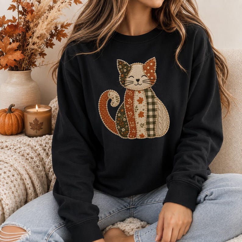 May include: A black long-sleeve sweatshirt featuring a central graphic of a cat composed of various patchwork-style fabric patterns in shades of orange, green, brown, and cream, including floral, leaf, polka dot, plaid, and cable knit textures.