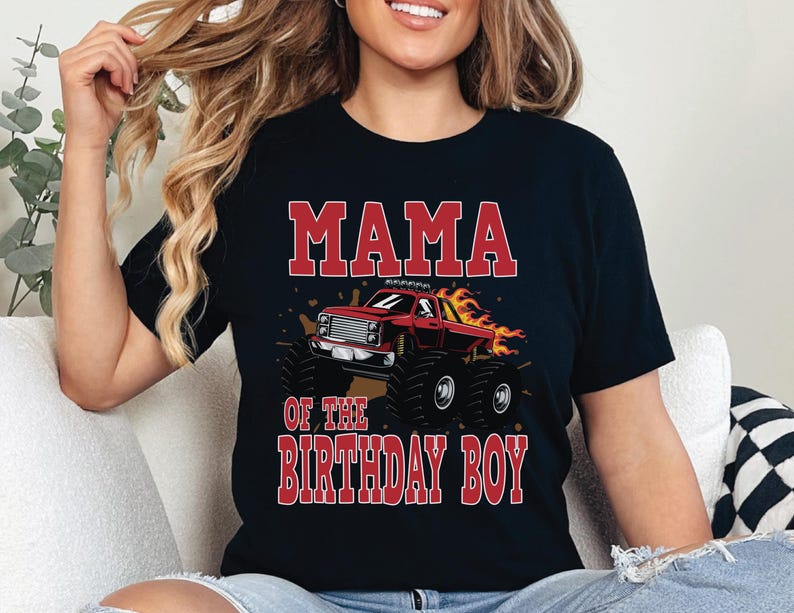 May include: Black t-shirt with the text "MAMA OF THE BIRTHDAY BOY" in red block letters. A red monster truck with flames is featured in the center. The shirt is a crew neck style.