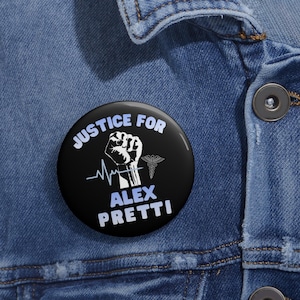 以下が含まれることがあります： 「JUSTICE FOR ALEX PRETTI」の白文字が入った黒いボタン。 握りこぶし、医療シンボル、白い心拍ラインが特徴です。