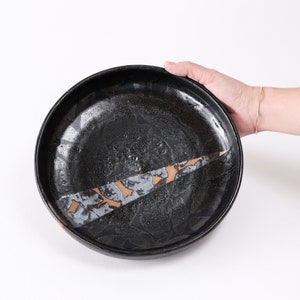 stunning handmade stoneware low serving bowl with a soft contemporary curve leading to the elevating foot ring. The bowl is finished in a metallic textured black glaze with a ray of unglazed part in the center.