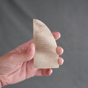 May include: A light brown, triangular-shaped piece of wood with a rounded edge. The wood has a smooth, polished finish.