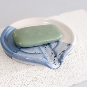 Puede incluir: Un jabonera de cerámica azul y blanca con una barra de jabón verde. La jabonera tiene un diseño único y ondulado.