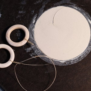 Puede incluir: Dos anillos de madera con una cuerda atada a cada uno. Los anillos están sobre una superficie negra con un círculo blanco en el centro.