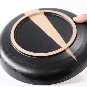 stunning handmade stoneware low serving bowl with a soft contemporary curve leading to the elevating foot ring. The bowl is finished in a metallic textured black glaze with a ray of unglazed part in the center.