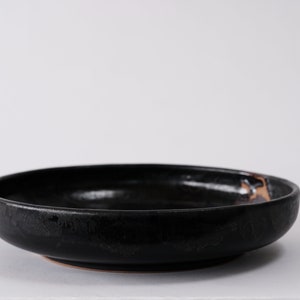 stunning handmade stoneware low serving bowl with a soft contemporary curve leading to the elevating foot ring. The bowl is finished in a metallic textured black glaze with a ray of unglazed part in the center.