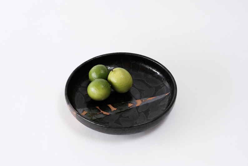 stunning handmade stoneware low serving bowl with a soft contemporary curve leading to the elevating foot ring. The bowl is finished in a metallic textured black glaze with a ray of unglazed part in the center.