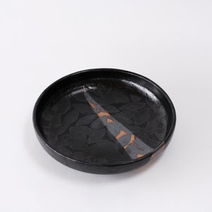 stunning handmade stoneware low serving bowl with a soft contemporary curve leading to the elevating foot ring. The bowl is finished in a metallic textured black glaze with a ray of unglazed part in the center.