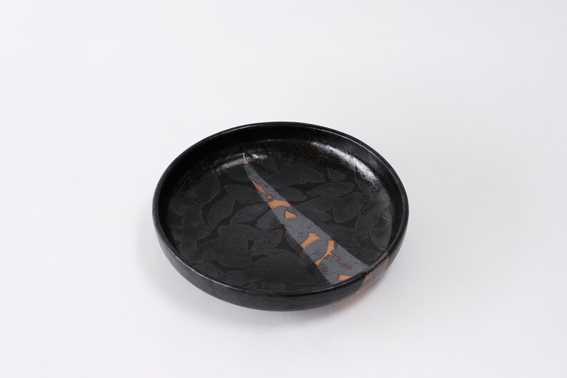 stunning handmade stoneware low serving bowl with a soft contemporary curve leading to the elevating foot ring. The bowl is finished in a metallic textured black glaze with a ray of unglazed part in the center.