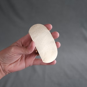 May include: A smooth, oval-shaped brass scraper tool.