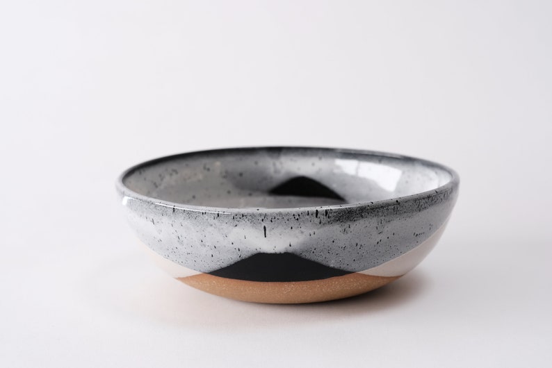 handmade tan stoneware ramen bowl. Two toned black and white overlapping glazes that creates a modern geometric pattern.