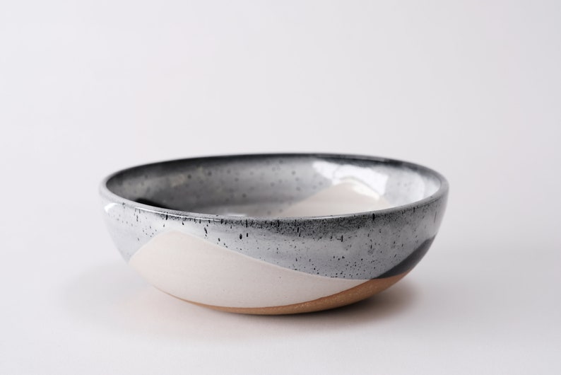 handmade tan stoneware ramen bowl. Two toned black and white overlapping glazes that creates a modern geometric pattern.