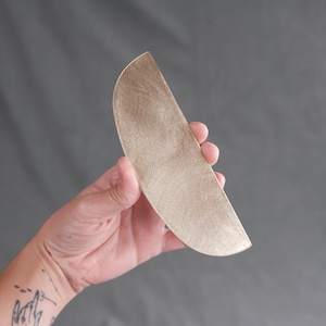 Puede incluir: Una bandeja de servir de metal de color dorado con forma de semicírculo.