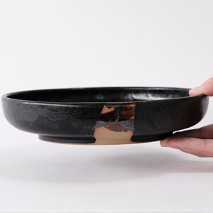 stunning handmade stoneware low serving bowl with a soft contemporary curve leading to the elevating foot ring. The bowl is finished in a metallic textured black glaze with a ray of unglazed part in the center.