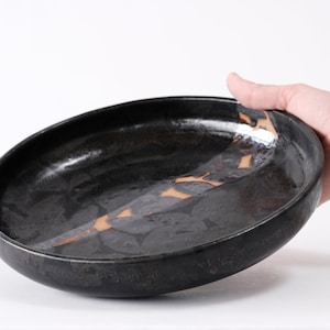 stunning handmade stoneware low serving bowl with a soft contemporary curve leading to the elevating foot ring. The bowl is finished in a metallic textured black glaze with a ray of unglazed part in the center.