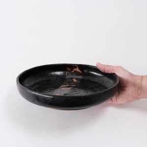 stunning handmade stoneware low serving bowl with a soft contemporary curve leading to the elevating foot ring. The bowl is finished in a metallic textured black glaze with a ray of unglazed part in the center.